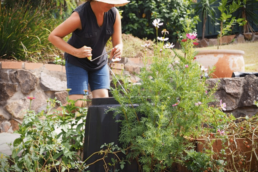 A woman using a compost screw to turn her compost within a black compost bin.