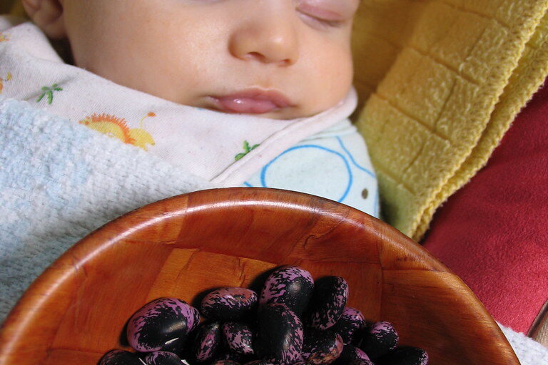 Sleeping baby Ashar beside a bowl of harvested dried beans