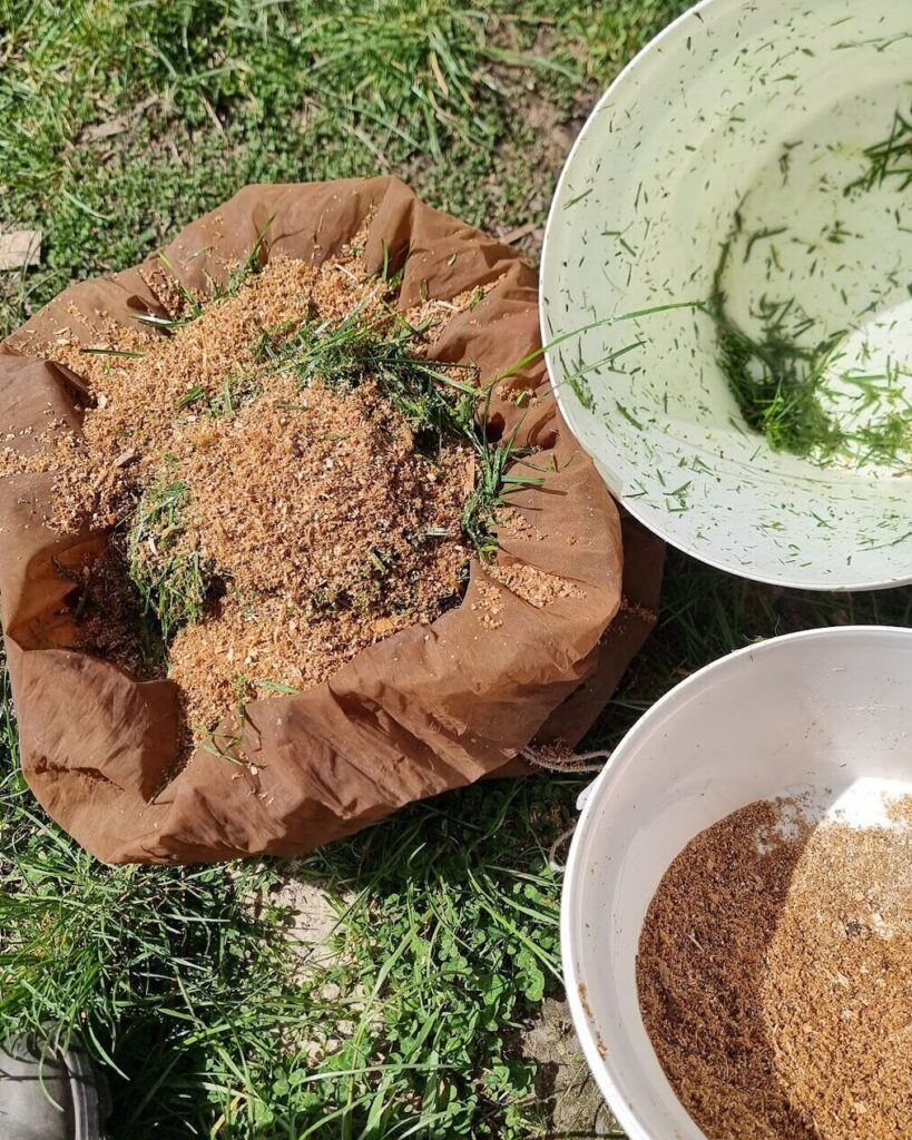 Grass clippings mixed with sawdust on an open cloth bag, with a bucket of each beside it