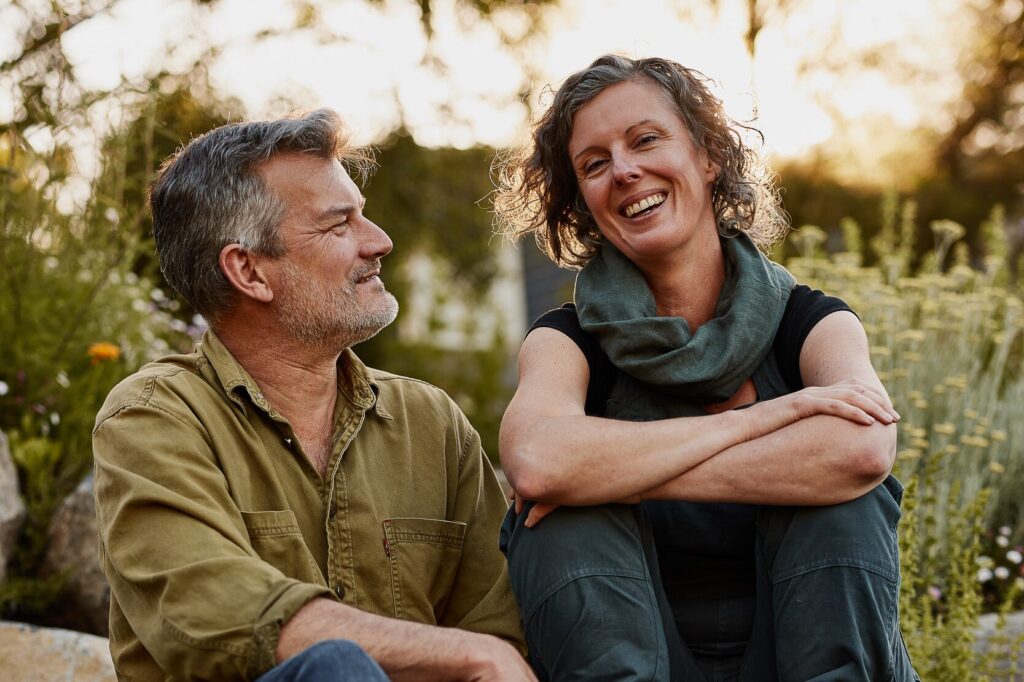 Kirsten and Nick sitting together on a rock in their garden at golden hour, Kirsten laughing and Nick smiling at her
